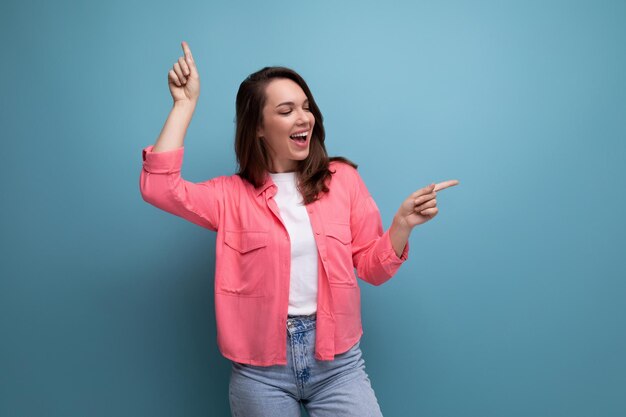 Cheerful brunette lady in a pink shirt and jeans points her finger at the infomation on a studio