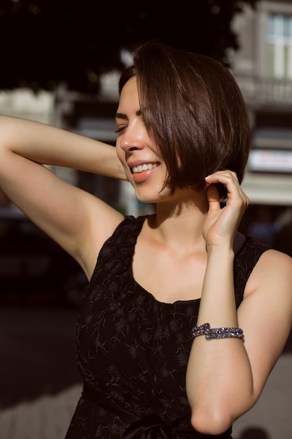 Cheerful brunette model with bronze tan posing on the street in a fashionable dress