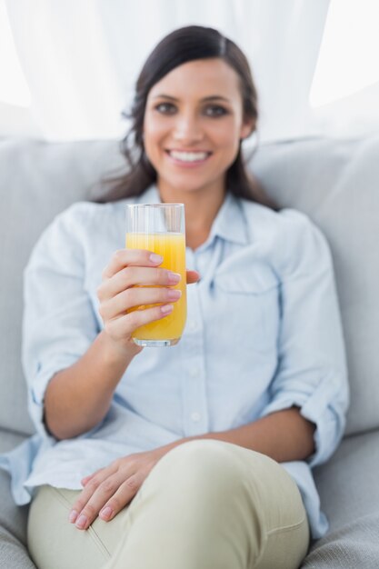 Photo cheerful brunette offering orange juice to camera