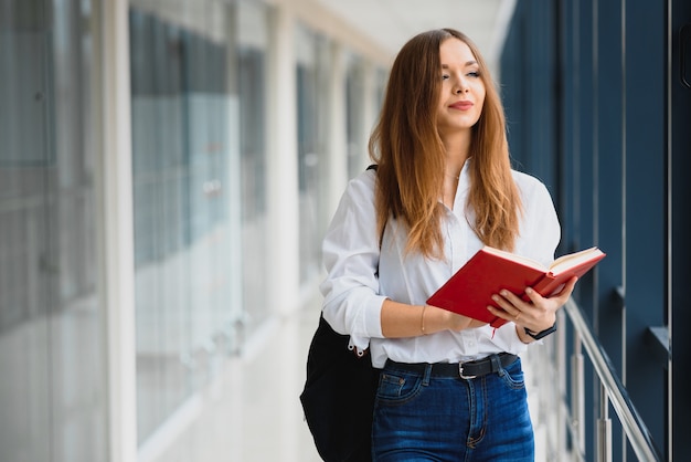 Cheerful brunette student girl with black backpack holds books in modern building