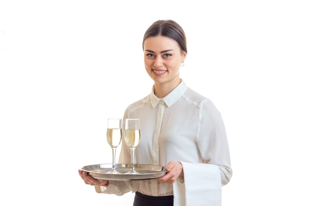 Cheerful brunette waitress smiles and hold a trey with champagne isolated on white background