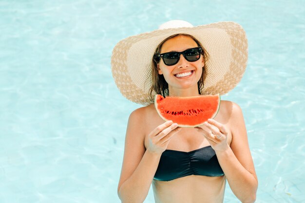Cheerful brunette woman in a black bikini holding a watermelon in her hands and smiling