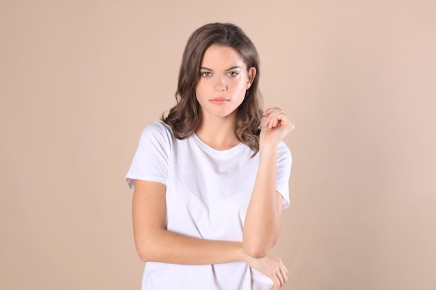 Cheerful brunette woman dressed in basic clothing looking at camera, isolated on beige background