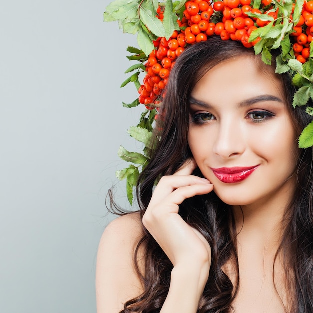 건강한 곱슬 헤어스타일 메이크업과 붉은 열매와 녹색 잎 초상화를 가진 쾌활한 갈색 머리 여성 패션 모델