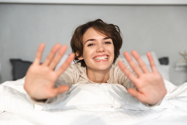 Веселая брюнетка женщина весело лежа на кровати у себя дома