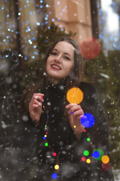 雪と色とりどりの花輪の近くの通りを歩く陽気なブルネットの女性