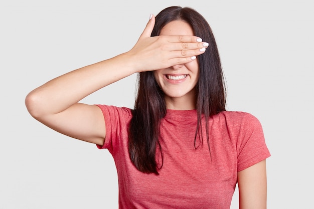 Cheerful brunette young European woman covers eyes with palm