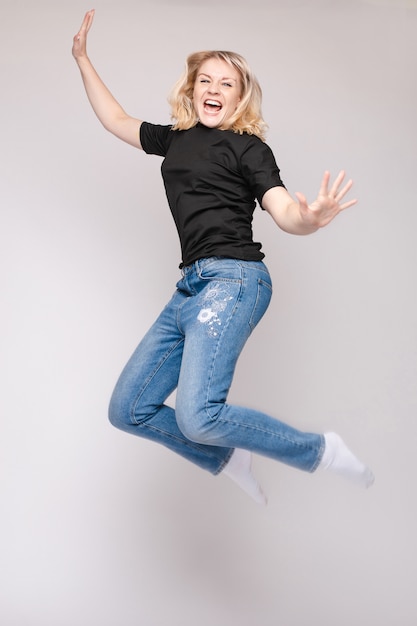 Cheerful brunette young woman in casual outlook jumping in mid air in studio.