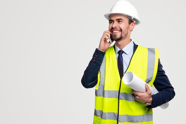 Cheerful builder with draft speaking on smartphone