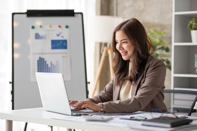 cheerful business lady working on laptop in office asian happy beautiful businesswoman in formal suit work in workplace attractive female employee office worker smile