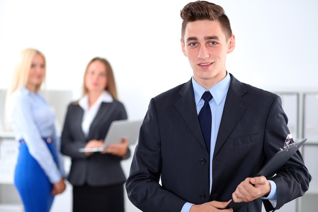 Cheerful business man in office with colleagues in the background sturtup team