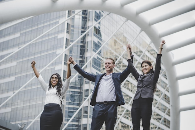 Photo cheerful business people standing with arms raised against metallic structure