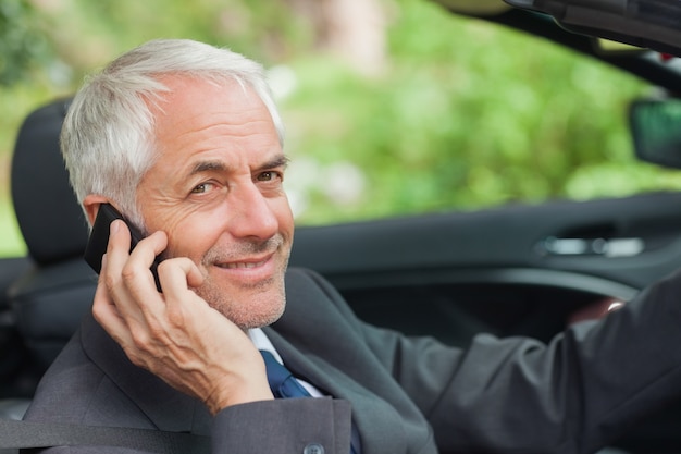 Cheerful businessman on the phone driving expensive cabriolet