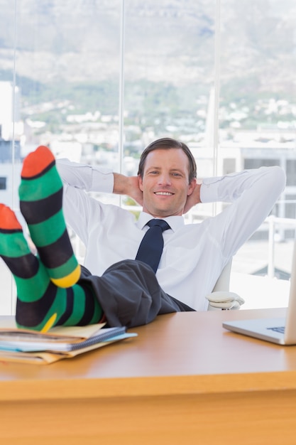 Cheerful businessman relaxing with feet on his desk