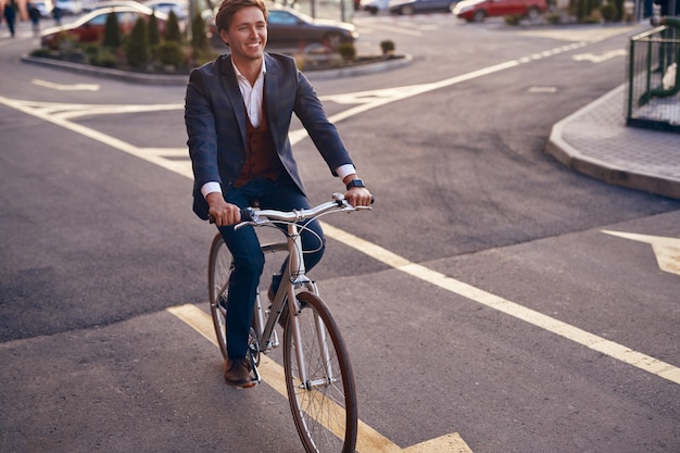 Cheerful businessman in suit riding bike down road