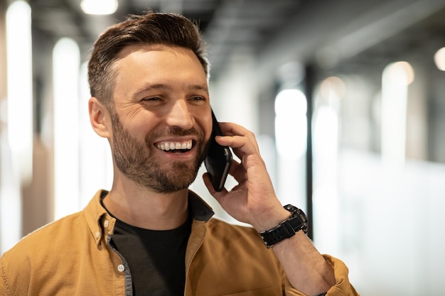 Cheerful businessman talking on cellphone looking aside standing in office