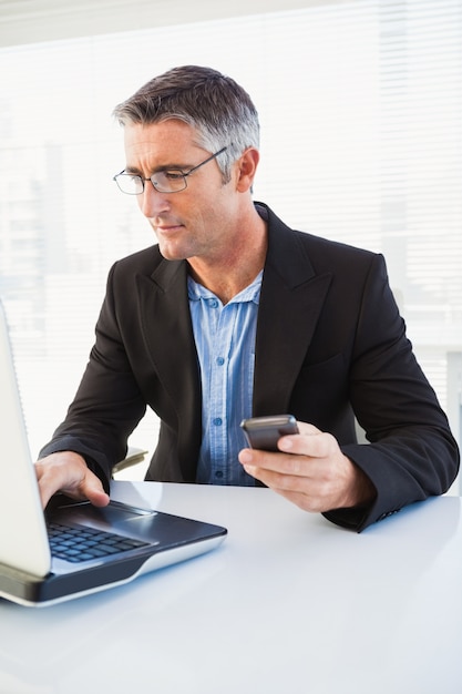 Photo cheerful businessman using laptop and holding smartphone