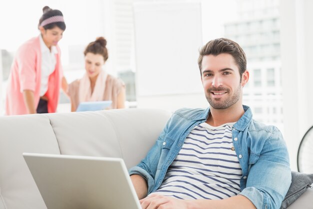 Cheerful businessman using laptop on sofa