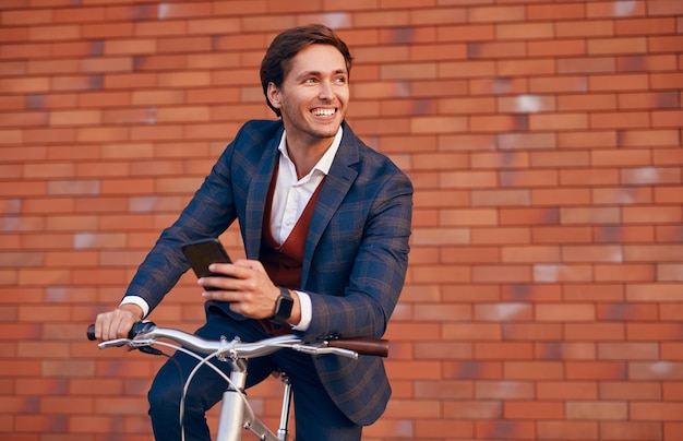 Cheerful businessman using smartphone on bicycle