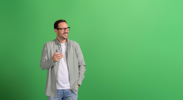 Cheerful businessman with hand in pocket looking away and using mobile phone over green background