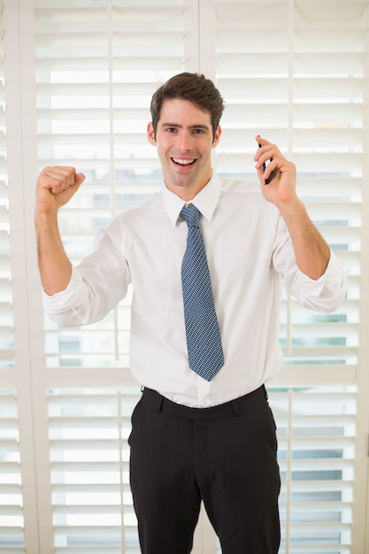 Cheerful businessman with mobile phone clenching fist in office