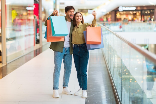 Cheerful buyers couple shopping having fun making selfie in mall