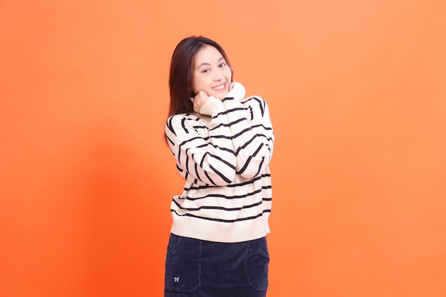 Cheerful casual Asian beauty woman both hands holding chin isolated on orange background natural mak