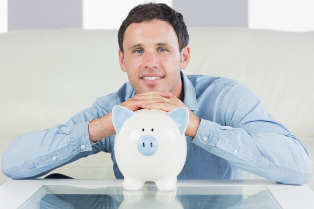 Cheerful casual man resting head on piggy bank