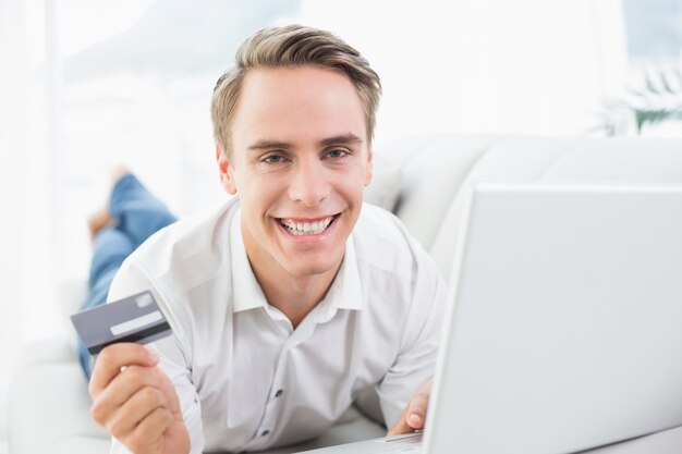 Cheerful casual young man doing online shopping on sofa