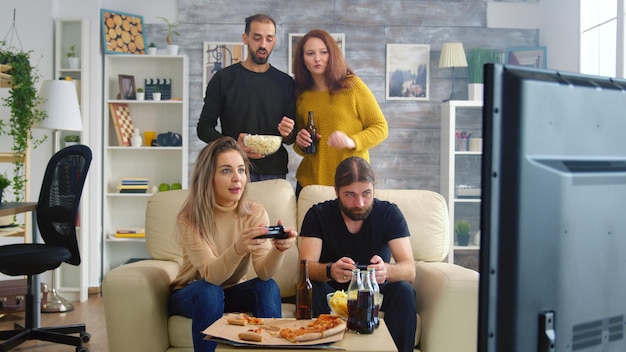 Cheerful caucasian friends playing video games on big tv in living room.