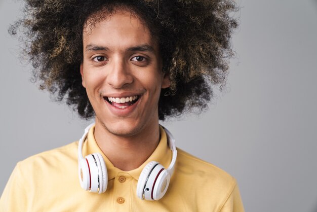  cheerful caucasian man with afro hairstyle wearing headphones smiling isolated over gray wall