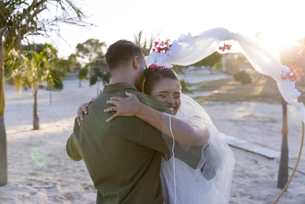 Photo cheerful caucasian newlywed couple embracing and standing at beach at wedding ceremony, copy space