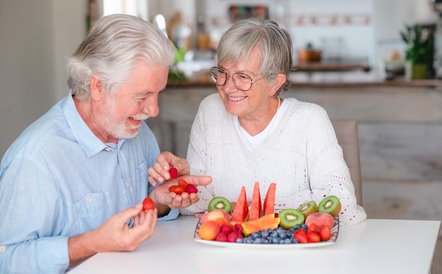 Foto coppia senior caucasica allegra che fa colazione a casa con il concetto di alimentazione sana di frutta fresca di stagione