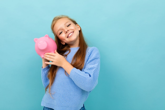 Cheerful charismatic schoolgirl posing with a piggy bank for money