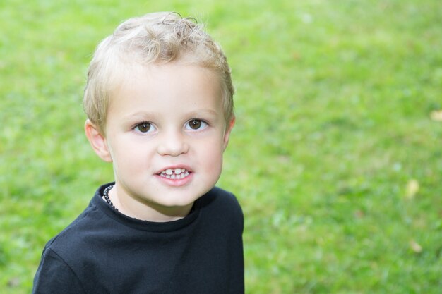 Cheerful child blond boy in green grass outdoor