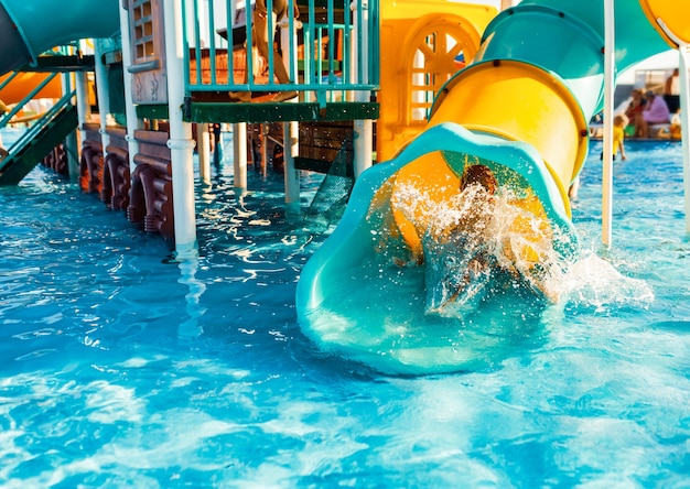 Un bambino allegro scende da un luminoso scivolo-tunnel in piscina e fa spruzzi