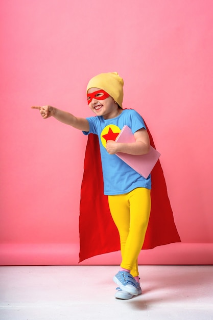 Cheerful child dressed in superhero costume and a hat with a book in his hands.