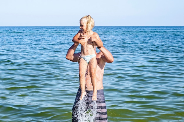 Cheerful child girl and dad are playing swimming in the sea.