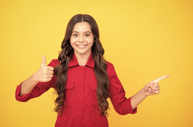 Cheerful child girl pointing finger on copy space with thumb up gesture success