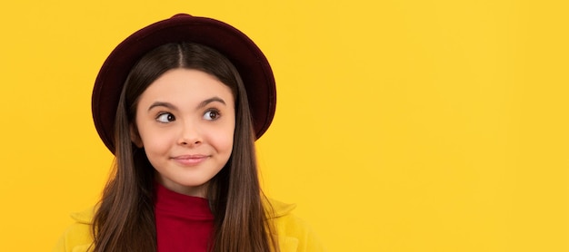 Cheerful child in hat and coat with autumn maple leaf on yellow background season Child face