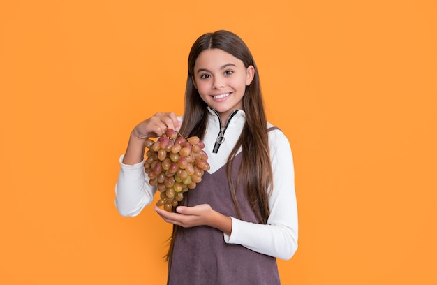 cheerful child hold ripe grapes fruit on yellow background