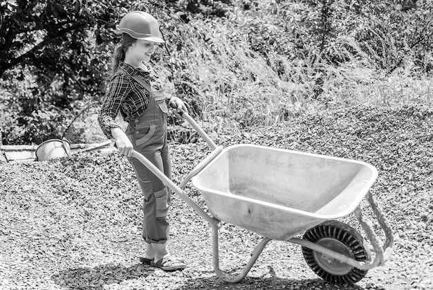 Foto lavoro minorile allegro che usa l'uniforme da costruzione e la carriera futura della carriola da costruzione
