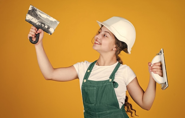 Cheerful child laborer using building uniform and plastering spatula equipment