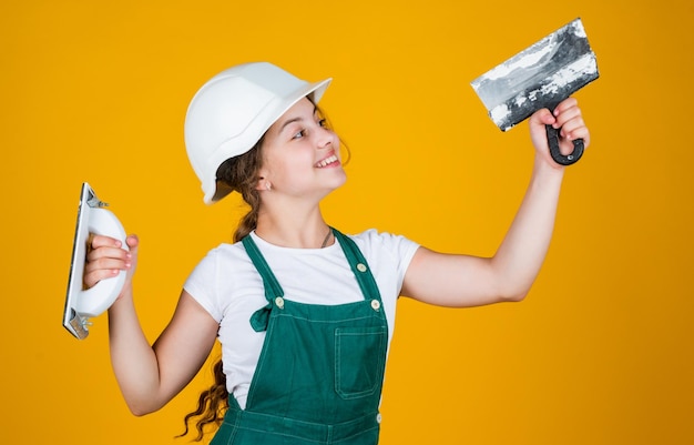 cheerful child laborer using building uniform and plastering spatula, equipment.