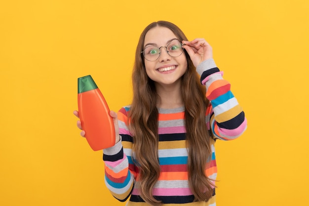 Cheerful child long hair in glasses presenting shampoo bottle advertisement