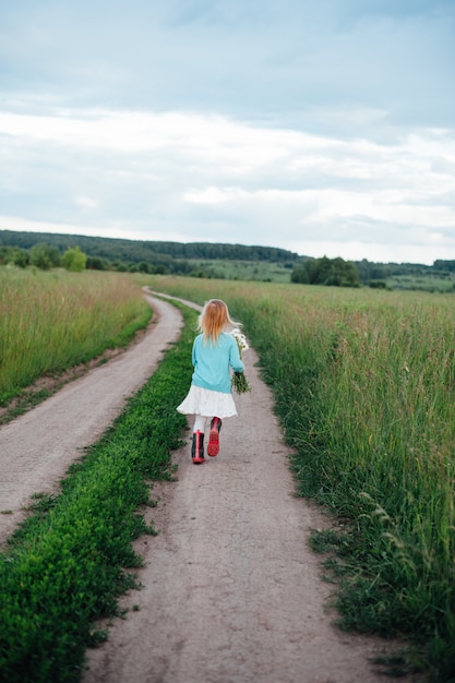 A cheerful child runs with a bouquet of daisies in boots