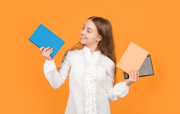 Cheerful child showing school book on yellow background back to school