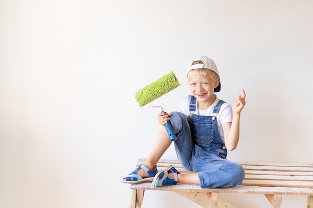 A cheerful child sits on a construction ladder in an apartment with white walls and a roller