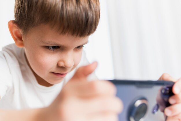 A cheerful child in a white T-shirt plays games on the phone at home. Happy boy looks at his smartphone.