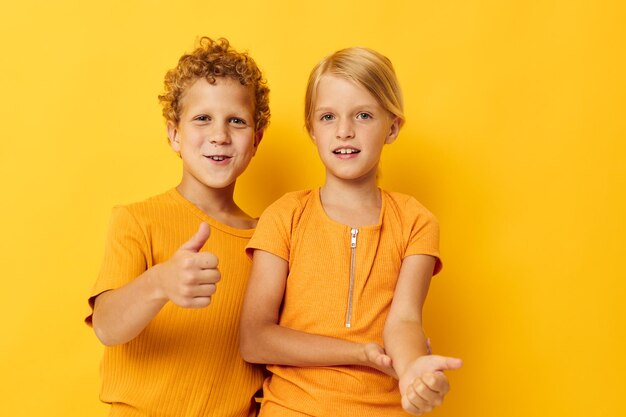 Cheerful children in yellow tshirts standing side by side childhood emotions yellow background unaltered